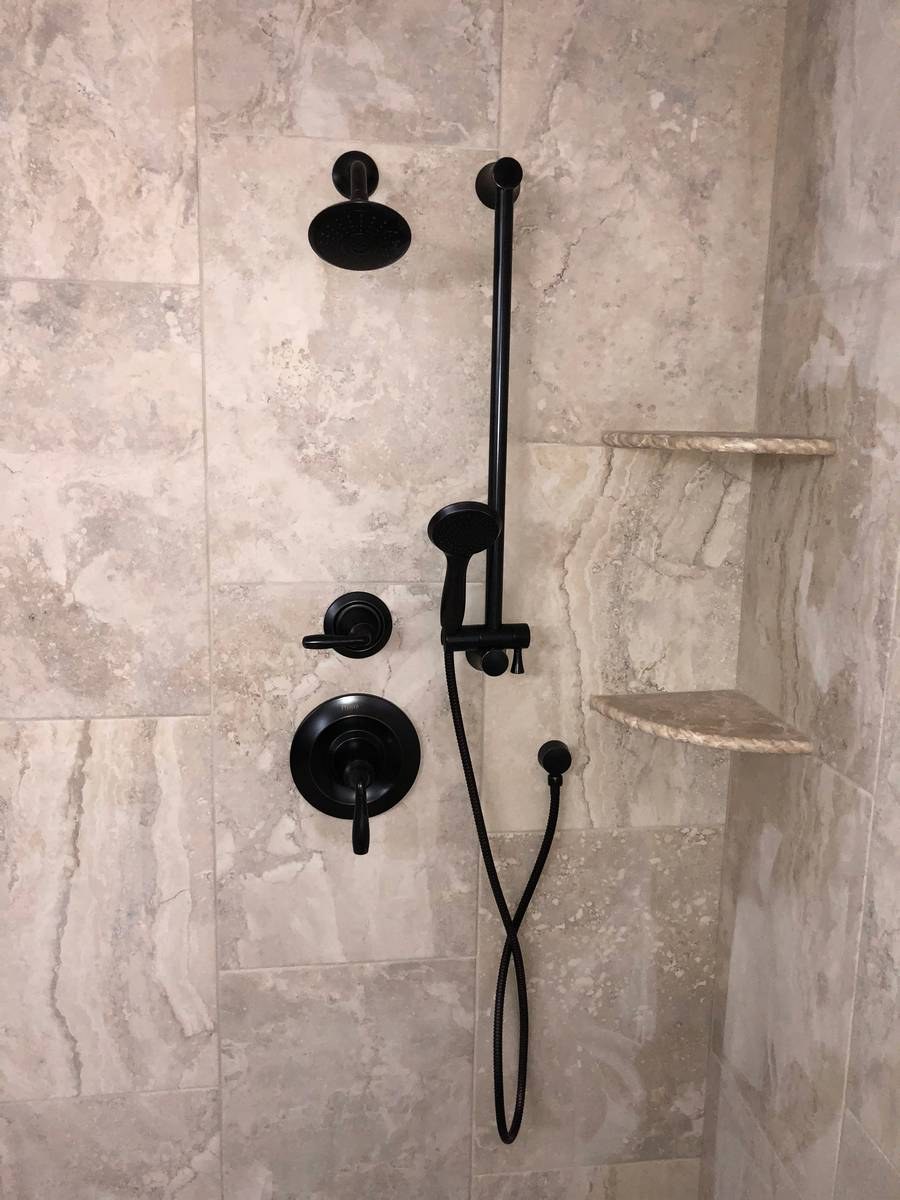 Walk-in shower with matte black fixtures and travertine stone tile walls