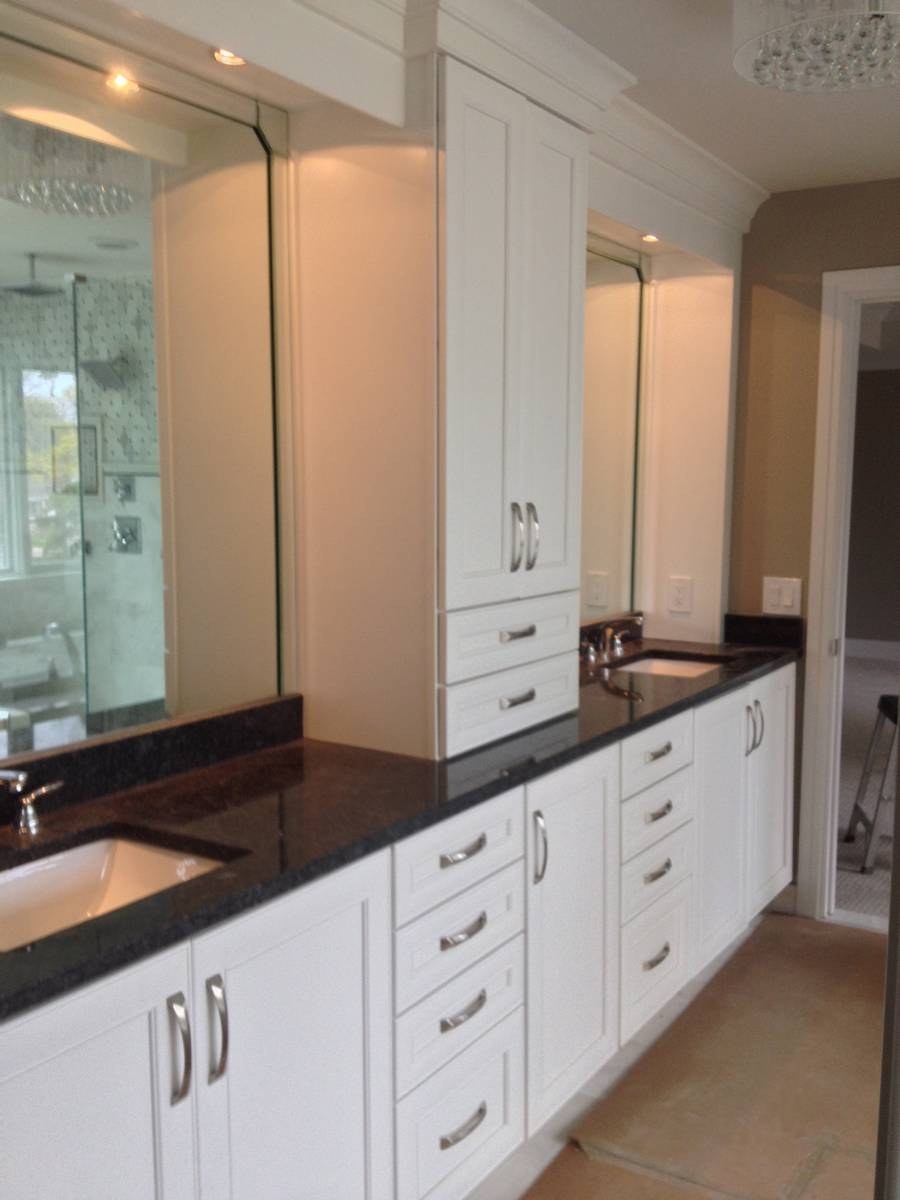 Primary bathroom with white dual vanity, black granite countertops, and center linen tower