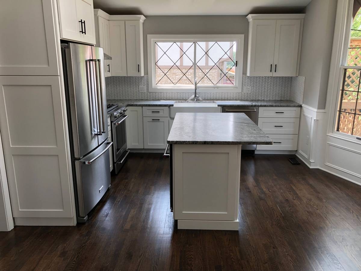 Wide white shaker kitchen with leaded-glass Tudor window, farmhouse sink, and dark oak floors