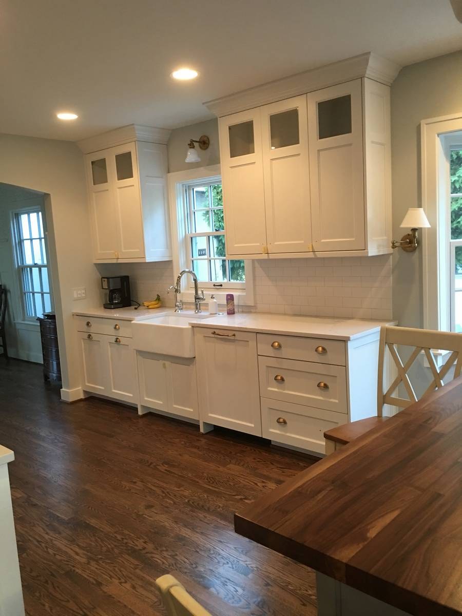Craftsman-style white kitchen with shaker cabinets, brass cup pulls, farmhouse sink, and butcher-block island
