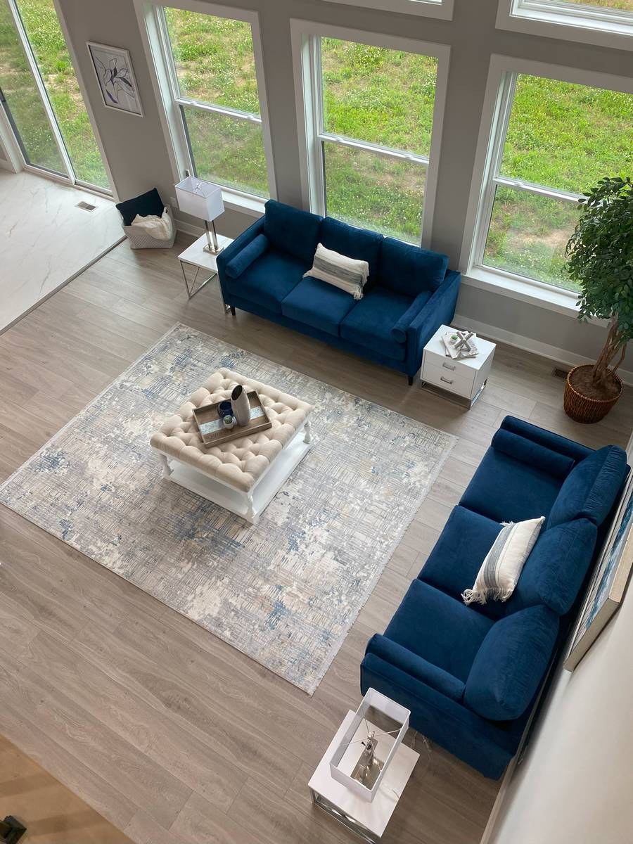 Double-height great room with floor-to-ceiling windows and blue velvet sofas, viewed from above