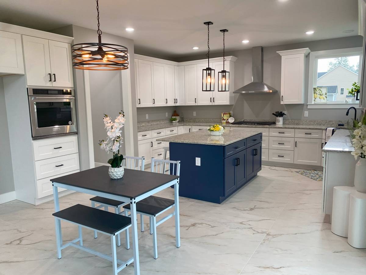 Custom new-build kitchen with white shaker cabinets, navy blue island, and calacatta marble floor tile