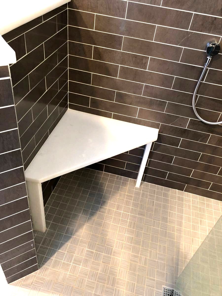 Marble corner bench inside dark subway tile walk-in shower