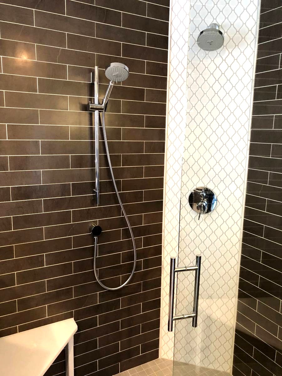 Walk-in shower interior with dark subway tile, arabesque accent, and glass door hardware