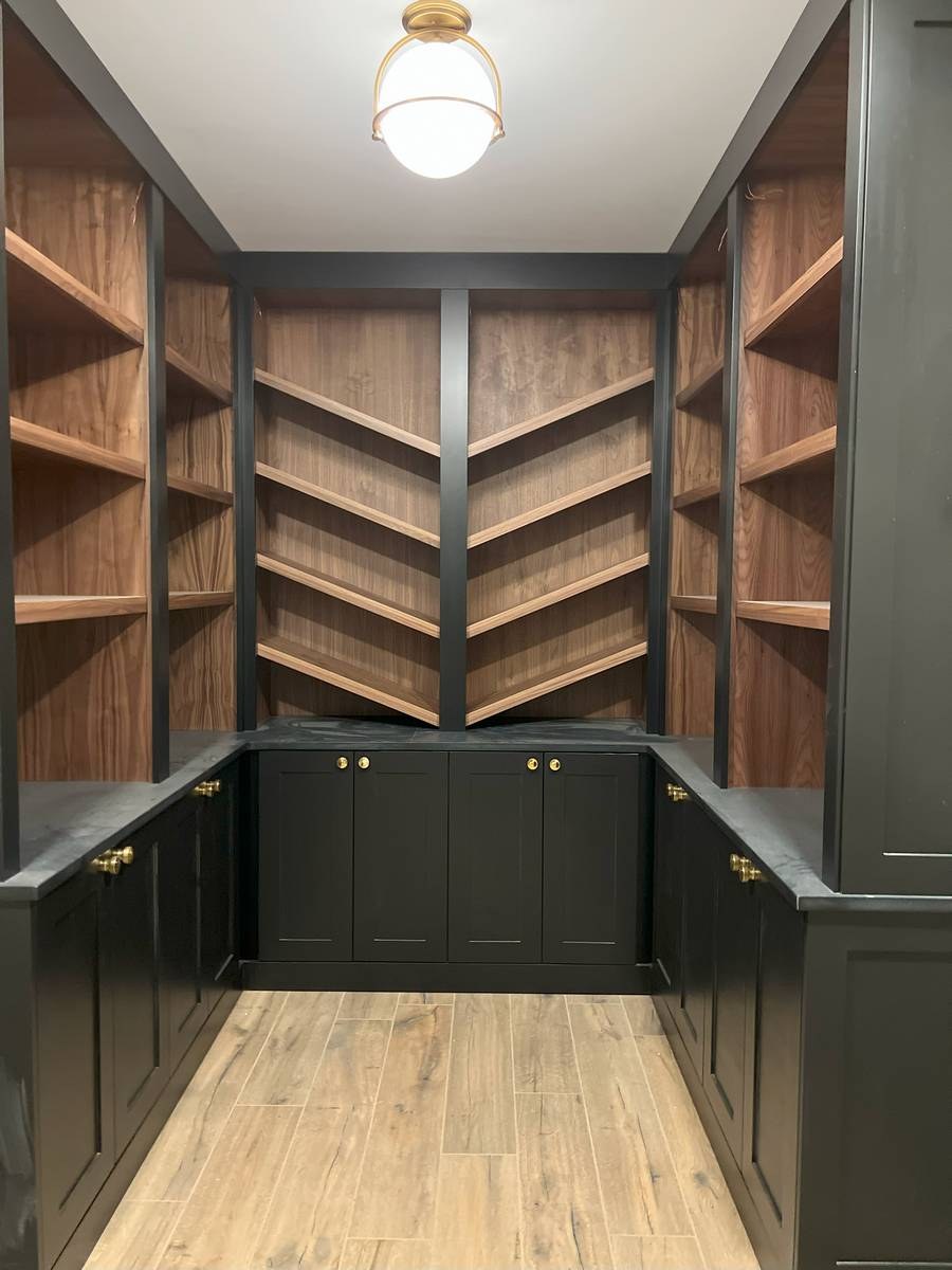 Walk-in butler's pantry with black shaker cabinets, walnut shelving, and brass knobs