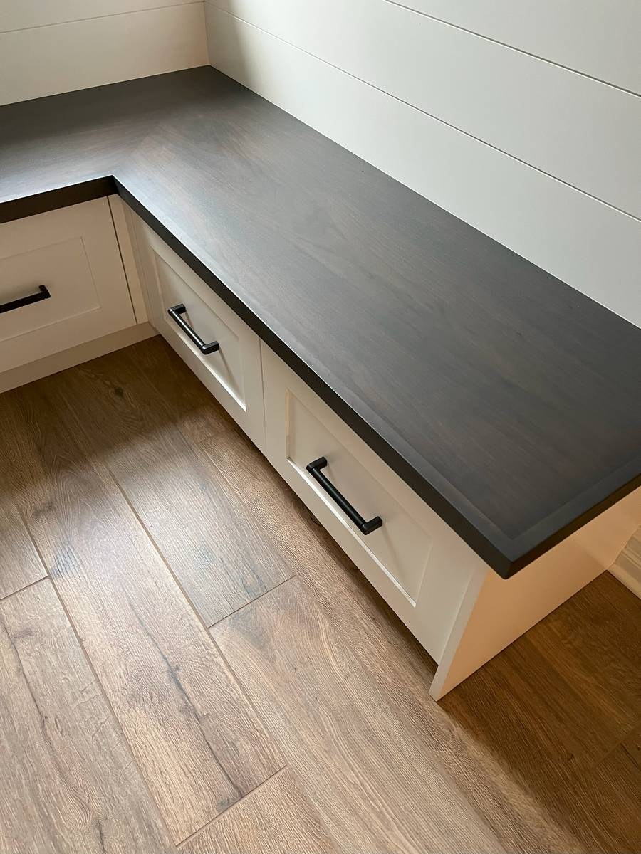 Mudroom storage bench with white shaker drawers, dark countertop, and shiplap wall