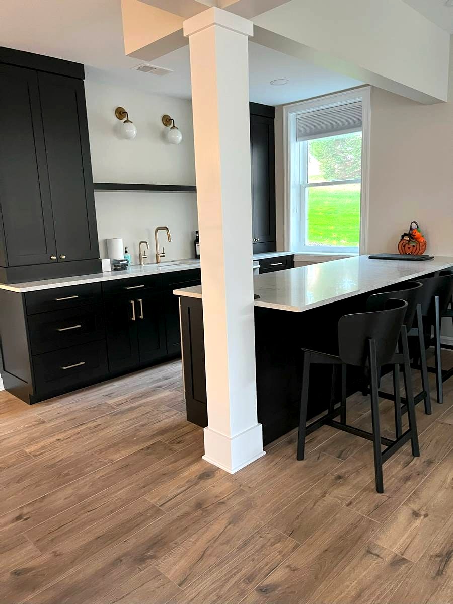 Black shaker wet bar with white quartz counters, brass faucet, and bar seating