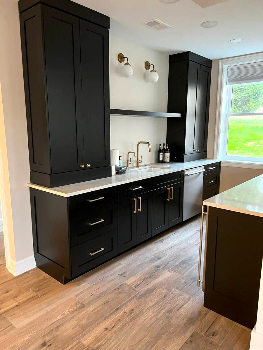 Black shaker wet bar with tall pantry towers, brass sconce lighting, and white quartz countertop