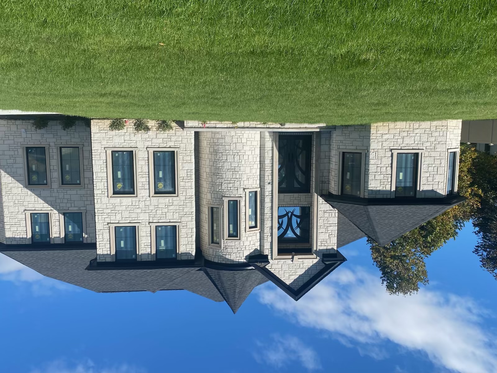 Completed custom two-story home with light stone exterior, dark roof, and manicured lawn