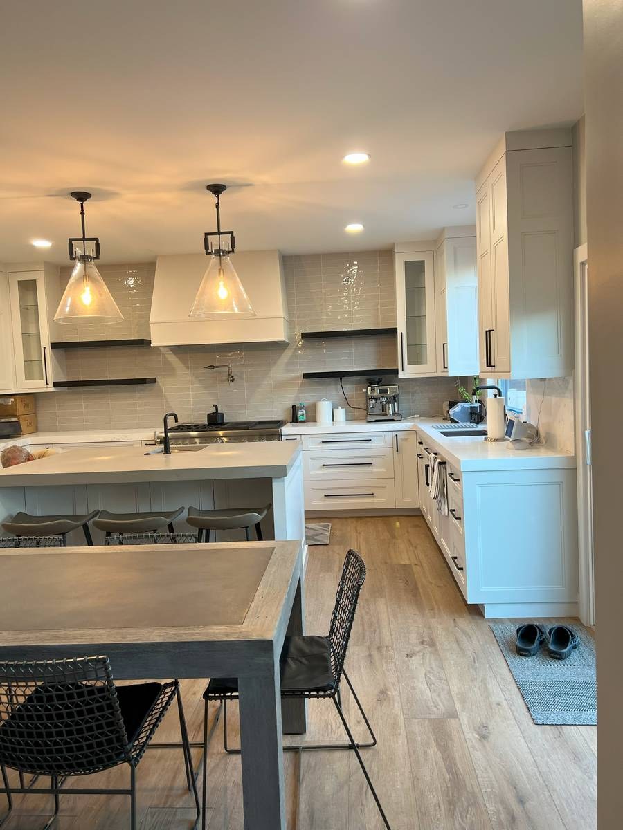 White kitchen with sage-green tile backsplash, glass pendant lights, and island with bar seating