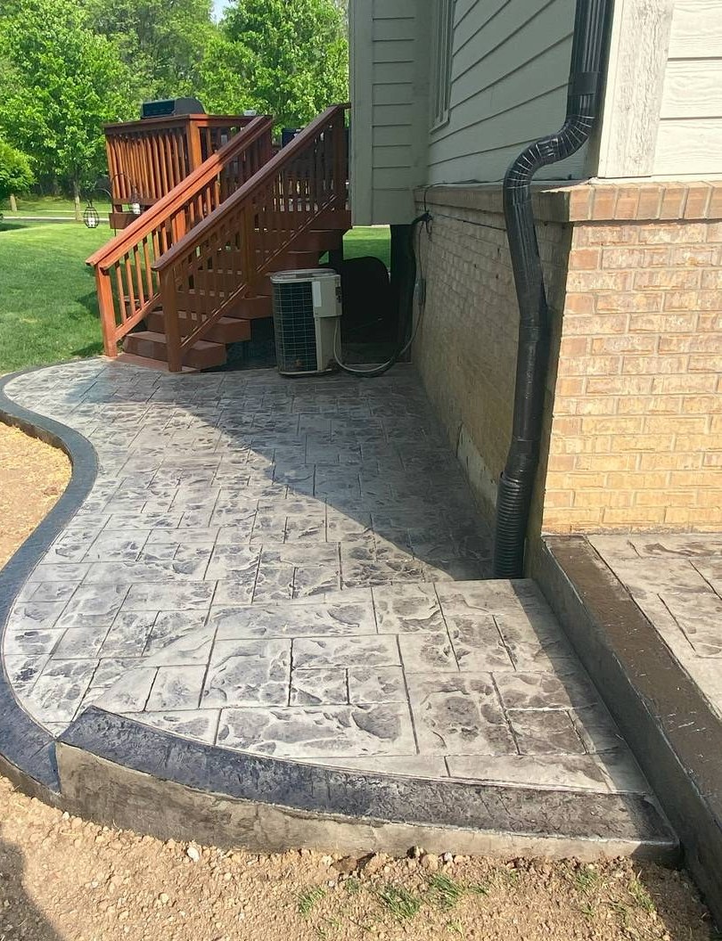 Stamped concrete curved walkway and patio with charcoal border alongside home exterior