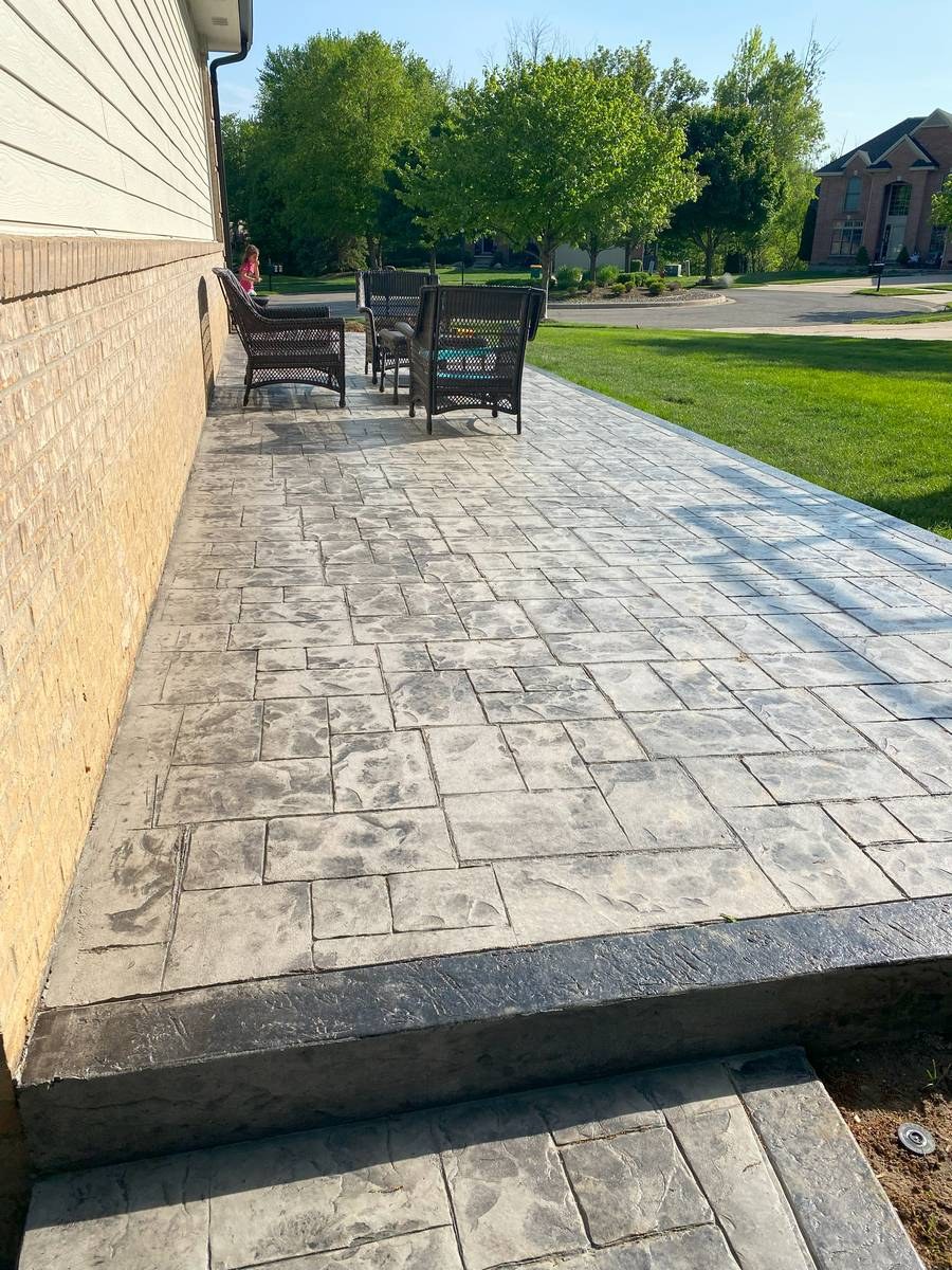 Wide stamped concrete patio with outdoor furniture, landscaping, and charcoal border detail