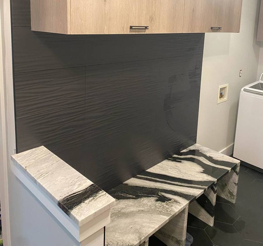 Laundry room renovation with white oak upper cabinets, dark tile accent wall, and dramatic marble countertop