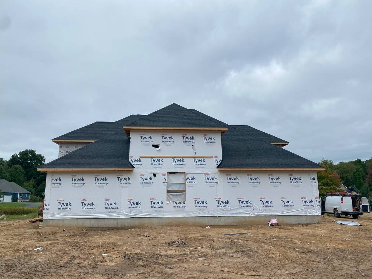 Ranch-style custom home fully dried in with dark shingle roof and Tyvek wrap