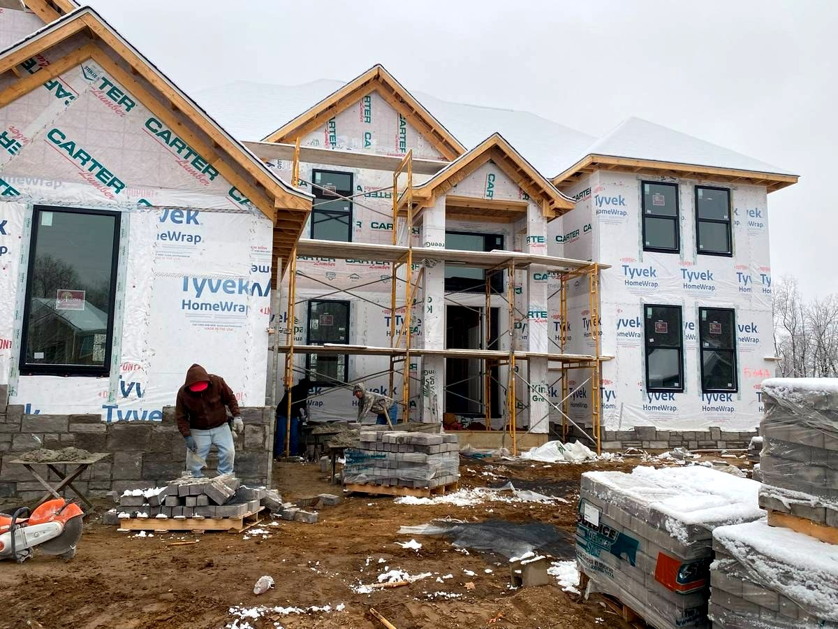 Two-story custom home with scaffolding during exterior siding installation in winter